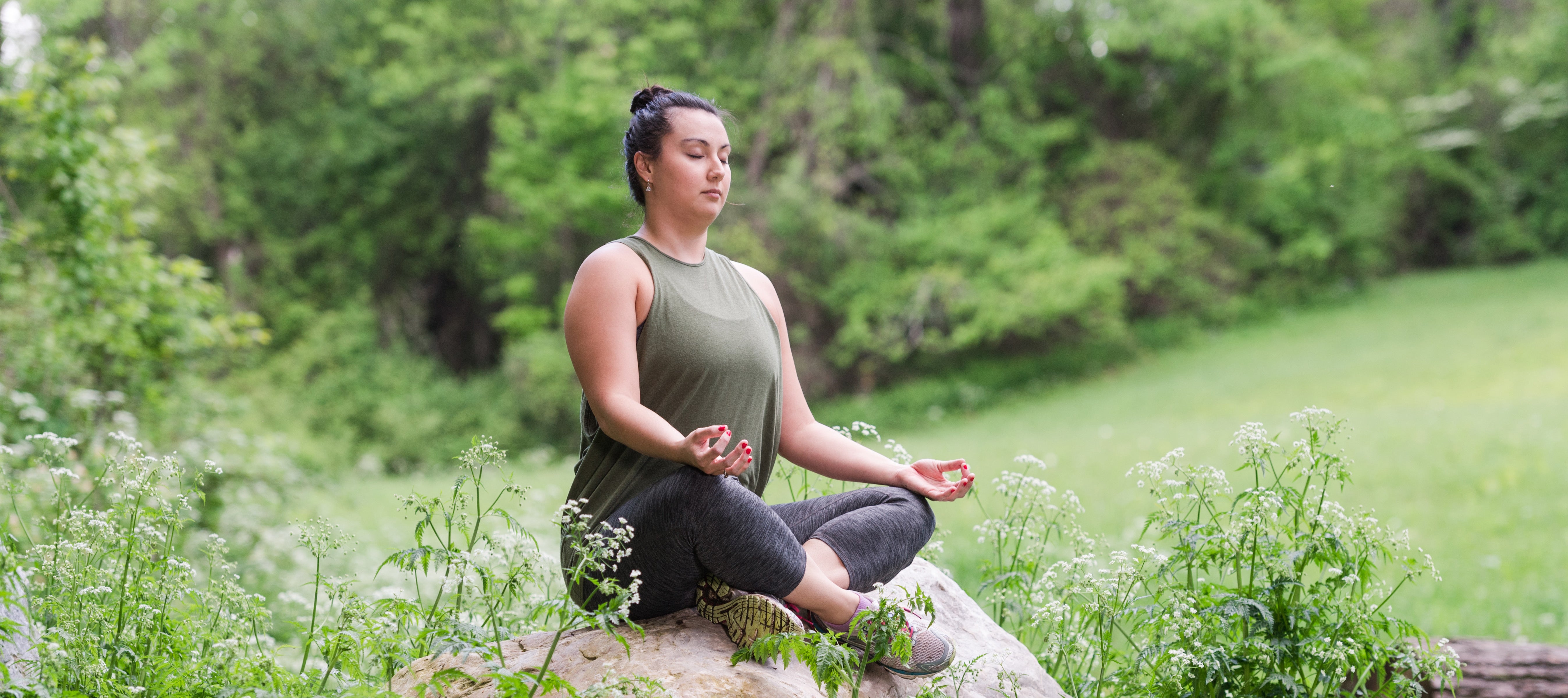 Ayurveda Self-Care Retreat Hero Woman sitting cross-legged on a rock meditating with eyes closed in the Spring.